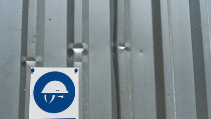 Safety helmet sign attention banner put in iron wall. A sign is warning to put a helmet on the construction site because of danger. Space for text.