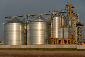 silver silos on agro manufacturing plant for processing drying cleaning and storage of agricultural products, flour, cereals and grain. Large iron barrels of grain. Granary elevator