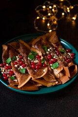 Chocolate pancakes or crepes with cranberries and nuts, served on a green plate. Winter holidays breakfast concept. Breakfast for Christmas and New Year. Dark background 