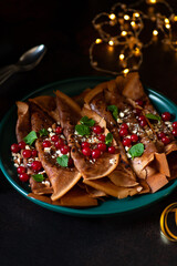 Chocolate pancakes or crepes with cranberries and nuts, served on a green plate. Winter holidays breakfast concept. Breakfast for Christmas and New Year. Dark background 