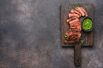 Medium rare steak sliced on black cutting board with pesto sauce. Dark brown food background