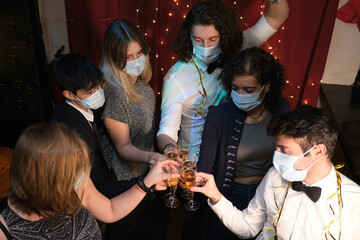 Friends wearing face masks at a Christmas party making a toast in a bar. Coronavirus new normal.