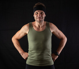 Fototapeta premium Handsome shirtless fitness man in gray shorts, smiling and posing against dark black background. Mild retouch, studio lighting.