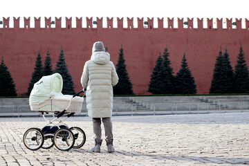 Woman with a baby stroller standing on Red square in Moscow on Kremlin wall background. Concept of...