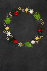 Christmas wreath decoration with winter holly, cedar cypress fir leaves and gold star decorations on grey grunge background. Festive composition for the xmas & solstice season.