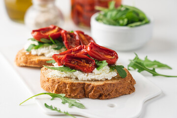 Bruschetta with sunny dried tomatoes and arugula. Delicious breakfast or wine snack. White background, close-up, top view