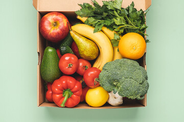 Cardboard box full of fresh vegetables and fruits on pastel green background. Food delivery concept. Healthy eating