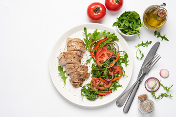 Baked chicken breast with vegetable salad. Chicken fillet with arugula, tomatoes and red bell pepper. White background, top view, copy space