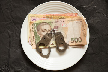 500 UAH Ukrainian and handcuffs lie on a white plate on a black background close up