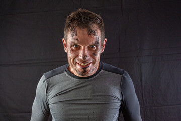 Handsome shirtless fitness man in gray shorts, smiling and posing against dark black background. Mild retouch, studio lighting.