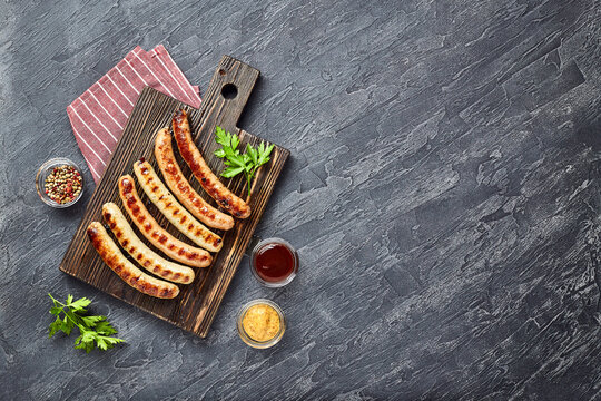Tasty grilled pork sausages with spice and herbs on wooden cutting board in a close up view on black background. Top view, flat lay.
