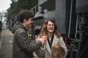 A guy and a girl are walking together among old steam locomotives
