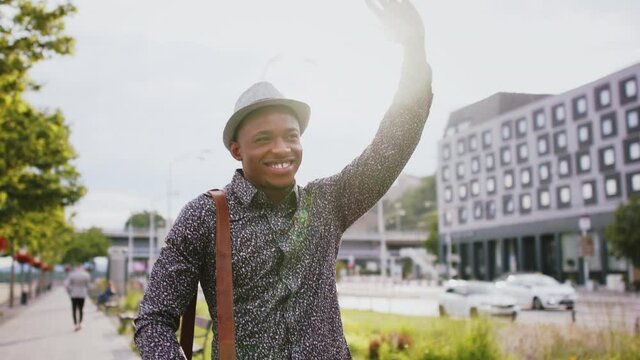 Cheerful young black man commuter outdoors in city, greeting somebody.