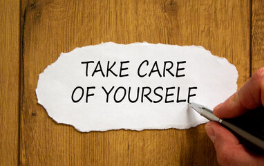 Male hand writing 'take care of yourself' on white paper on wooden table. Business and healty...
