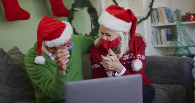Happy senior caucasian couple celebrating christmas wearing face maska and santa hats