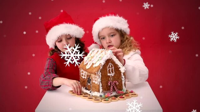 Animation of two girls in santa hats decorating gingerbread house