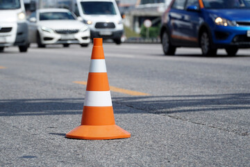 Road cone stands on the road against the backdrop of fast-moving cars.