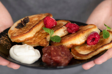 Breakfast with pancakes on plates, sour cream and pavidl. Pancakes are on a white table and the guy is holding in his hands.