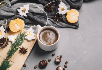 Home Christmas comfort, a Cup of hot espresso coffee on the table with a garland in the shape of a Christmas tree, tangerines, warm clothes