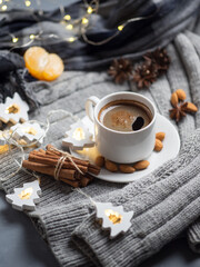 Home Christmas comfort, a Cup of hot espresso coffee on the table with a garland in the shape of a Christmas tree, tangerines, warm clothes