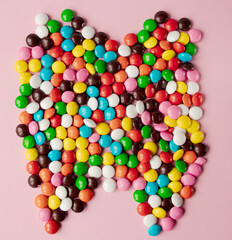 Obraz premium Tooth of chocolate multicolored candies flat lay view on pink background. Tooth made from candies.