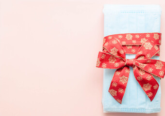 medical protective face masks as a gift with a red ribbon on a pink background. Christmas and New Year 2021 decor. Holidays self-isolation and coronavirus pandemic concept
