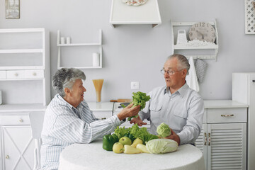 Couple in a kitchen. Grandparents sitting at home. Woman with vegetables