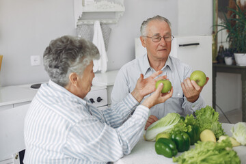 Couple in a kitchen. Grandparents sitting at home. Woman with vegetables