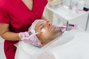A young man is undergoing a cosmetic facial peeling procedure. Cosmetology and rejuvenation