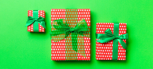 wrapped Christmas or other holiday handmade present in paper with green ribbon on green background. Present box, decoration of gift on colored table, top view