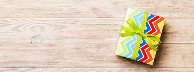 Beautiful gift box with a colored bow on the yellow wooden table. Top view banner with copy space for you design