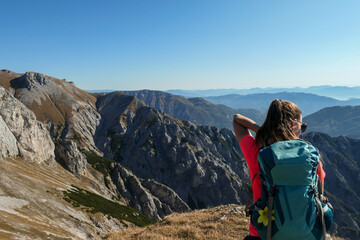 Naklejka premium A woman with big blue backpack enjoying the view on valley from top of a mountain in Hochschwab region in Austrian Alps. The flora overgrowing the slopes is turning golden. Freedom. She is happy
