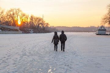 Couple walking across a frozen lake in the background of the sunset
