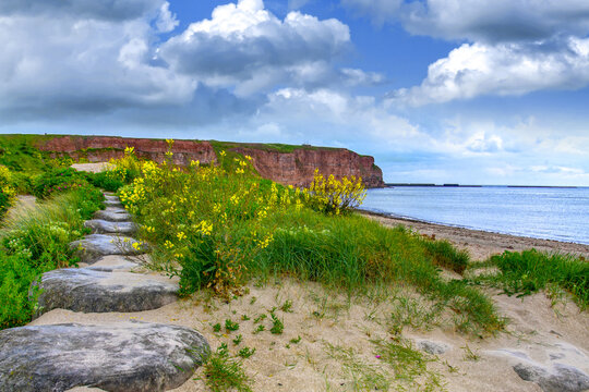 Insel Helgoland - Steinweg am Nordstrand / Blick auf die Nordsee und die roten Felsen vom Strand aus mit schönen Wolken im Hintergrund.