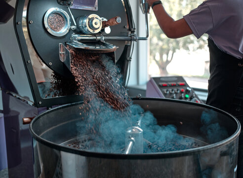 Roast some coffee. Process of freshly roasted coffee beans from a coffee roaster machine being poured into the cooling cylinder. Motion blur on the beans. Horizontal shot