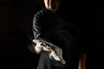 Chef hands cooking dough on dark background. chef throwing up dough for pizza. Chef Making dough. flour splash. Cooking bread. Kneading the Dough