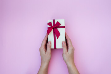 Gift box in the hands of a girl with a natural manicure on a pink background with a copy of the space. Christmas, New year, birthday, Valentine's day greetings concept.