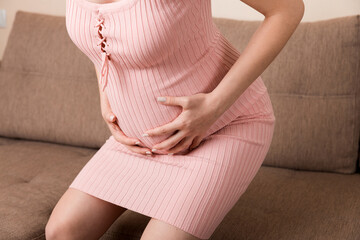 Pregnant Lady Having Massaging Lower belly Sitting On Sofa Indoor. Pregnancy Problems Concept. Maternity healthcare