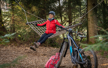 nice senior woman resting in a hammock during a mountain bike trip in a forest in the Allgaeu