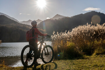 senior woman with electric mountain bike in bright backlit sun on the shore of lake Weissensee near...