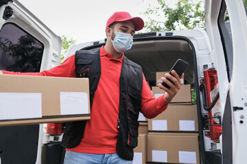 Delivery man with package and smartphone or digital scanner while wearing protective face mask at...