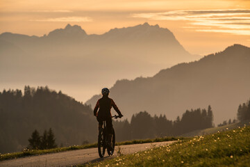 active woman riding her electric mountain bike at sunset in front of the awesome silhouette of Mount Saentis, Appenzell switzerland
