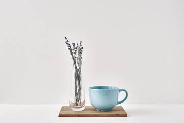 A vase with lavender and a mug stand on a wooden stand on a white background. Minimalism, eco-materials in the interior decor. Copy space, mock up.