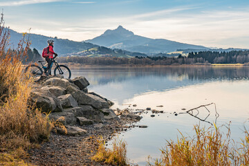 nice senior woman with electric mountain bike enjoying the view over autumnal lake Gruentensee in the Allgaeu alps near Nesselwang, Bavarian Alps, Germany