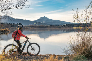 Obraz premium nice senior woman with electric mountain bike enjoying the view over autumnal lake Gruentensee in the Allgaeu alps near Nesselwang, Bavarian Alps, Germany