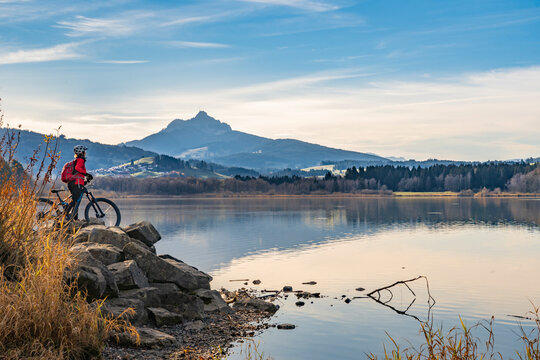 nice senior woman with electric mountain bike enjoying the view over autumnal lake Gruentensee in the Allgaeu alps near Nesselwang, Bavarian Alps, Germany