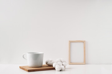 Frame, cotton and a cup on a wooden board, white background. Mock up, copy space. Folk.
