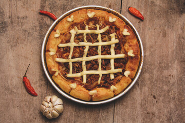 Top view of pizza with beef and cream cheese surrounded by chilies and garlic served on wooden table