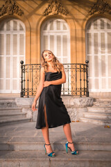Fototapeta na wymiar Lifestyle, Caucasian blonde in a glamorous dress and black heels in a rustic house. Young model posing next to the stairs of the beautiful building