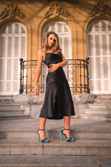 Fototapeta na wymiar Lifestyle, Caucasian blonde in a glamorous dress and black heels in a rustic house. Perched next to the stairs of the beautiful building